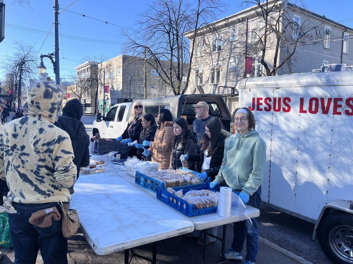 Volunteers handing out food beside the Jesus Loves You trailer on the Downtown East Side
