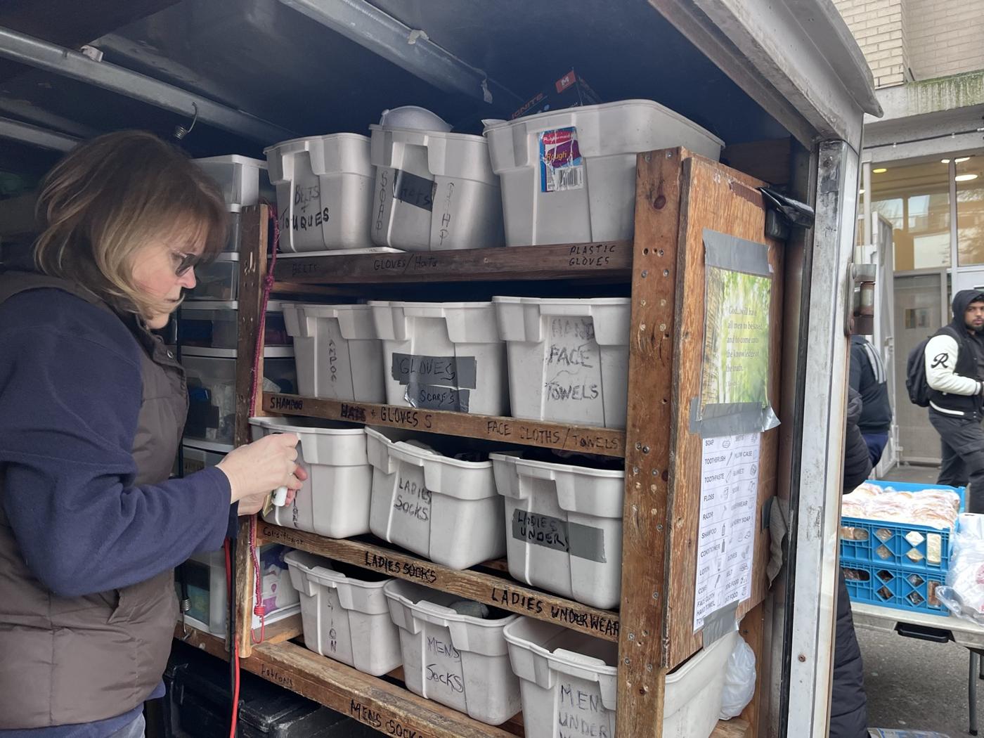 A volunteer stocking labelled bins on shelves inside the trailer